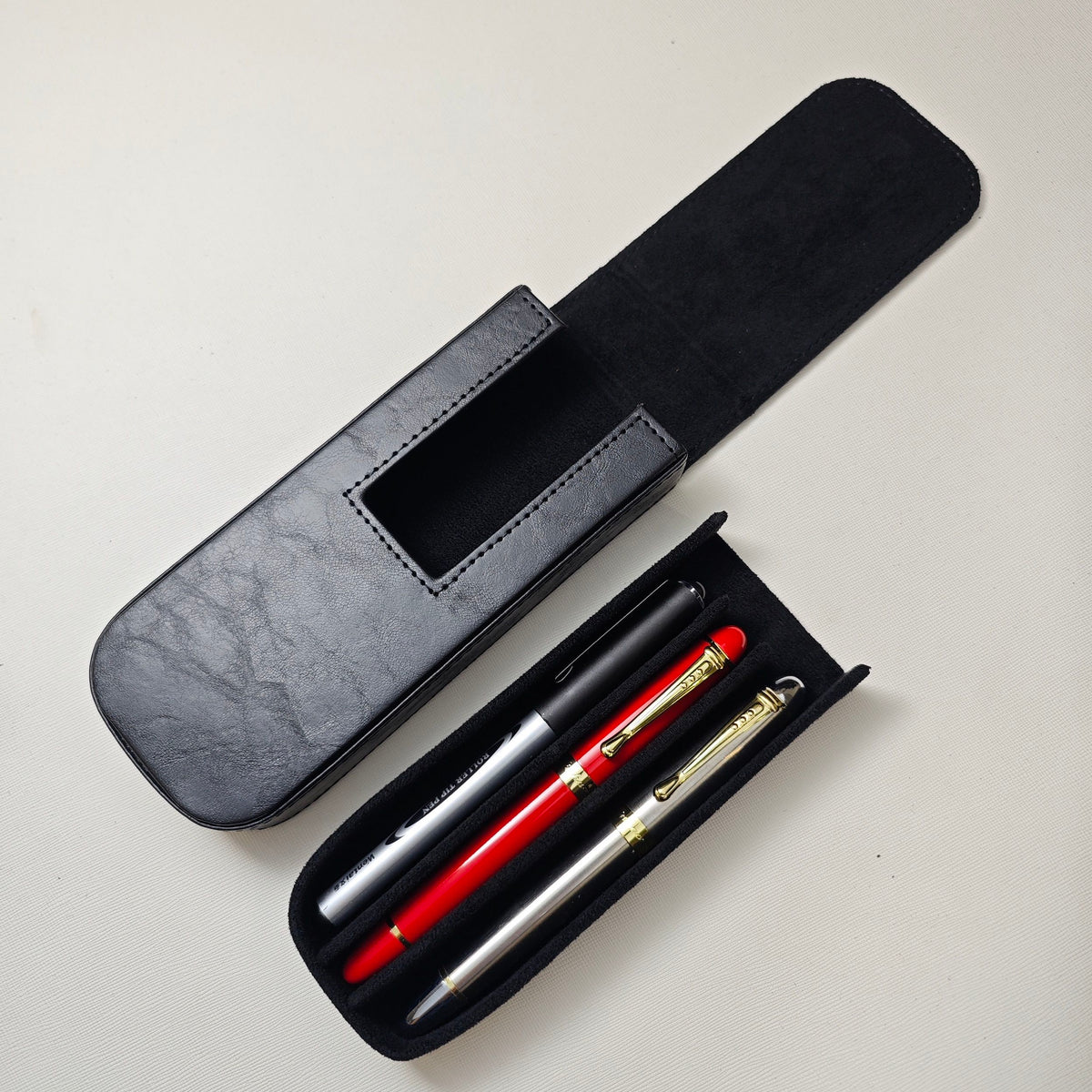 Open black leather pen case with 3 pens in tray